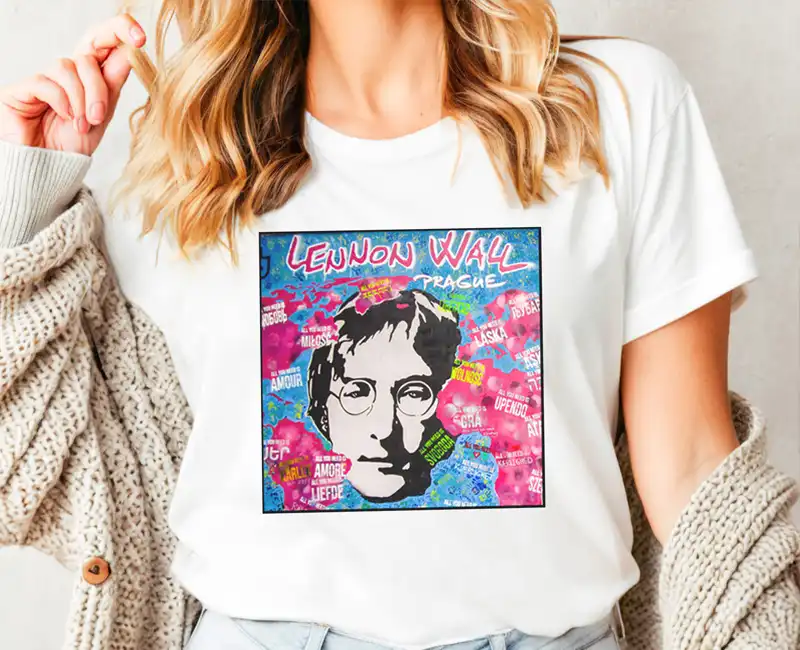A stylish white t-shirt worn by a female model, featuring authentic Lennon Wall art with a large John Lennon stencil surrounded by vibrant graffiti.