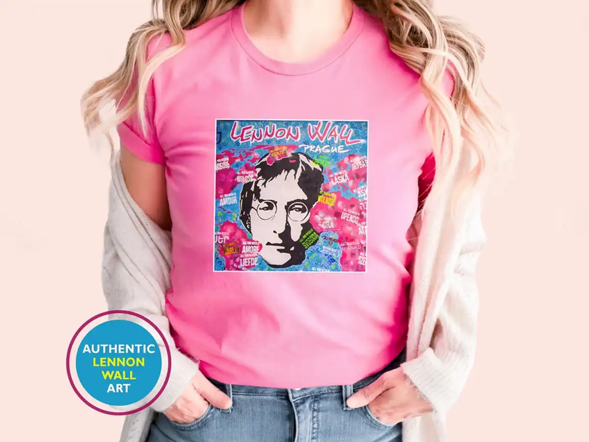 Female model wearing a pink t-shirt featuring authentic Lennon Wall Art with a large stencil of John Lennon surrounded by colorful graffiti in Prague.