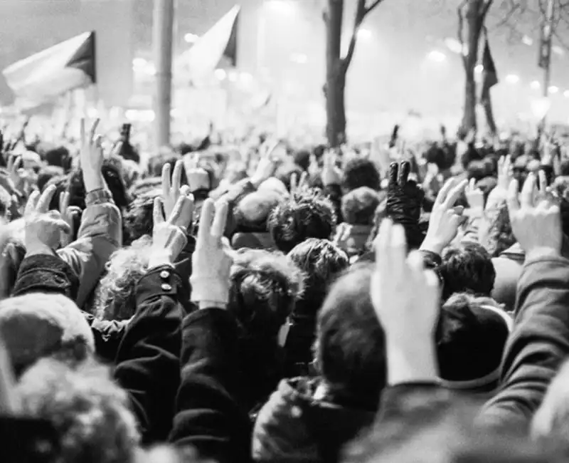 People raising their hands and fingers in the peace symbol during the Velvet Revolution in Prague, 1989, protesting on Václavské náměstí. The image captures the spirit of the revolution and its peaceful protest for change.